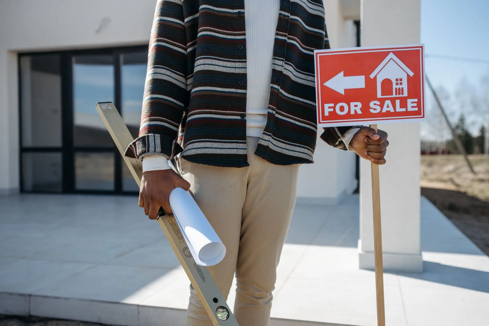 Vendeur tenant un panneau de vente et des plans devant une maison neuve
